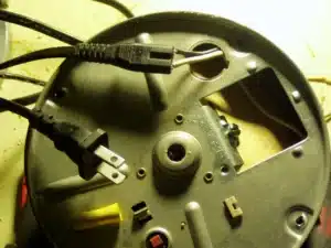 Underside of a garbage disposal with the power cord and wiring plate