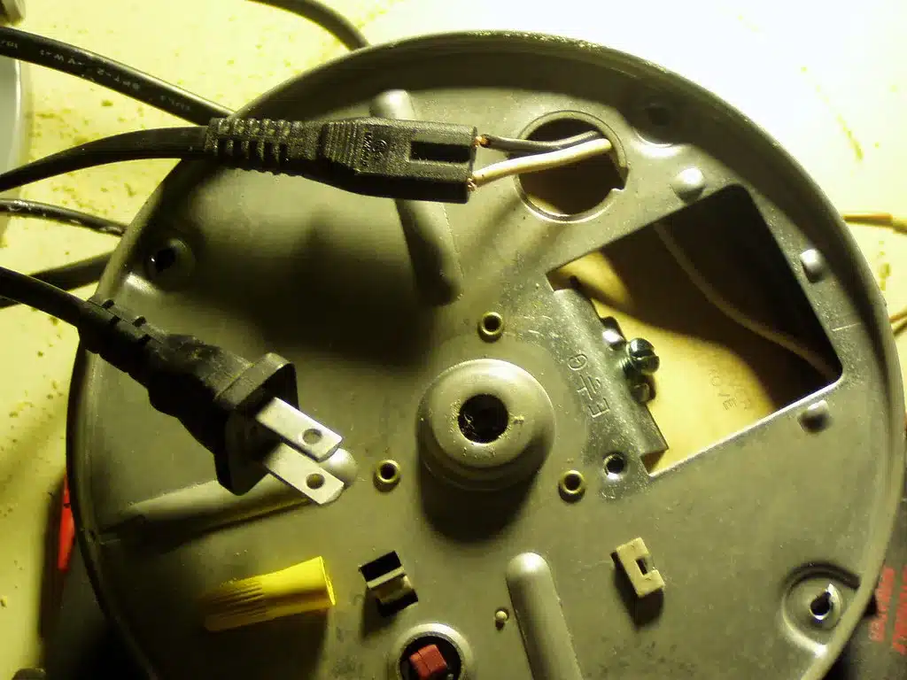 Underside of a garbage disposal with the power cord and wiring plate