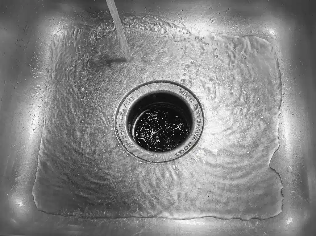 Water running into a kitchen sink drain with a garbage disposal