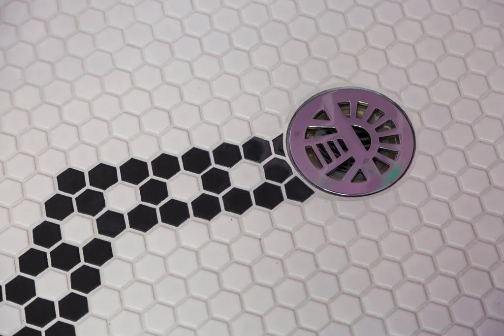 Mosaic tile shower pan sloping to a round drain